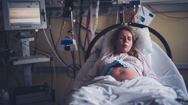 Eine schwangere Frau liegt in einem Krankenhausbett und hat ofensichtlich Wehen.