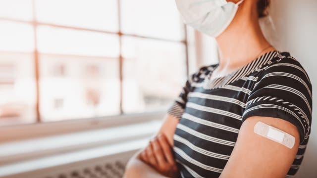 Frau mit Impfpflaster auf dem Arm blickt aus dem Fenster