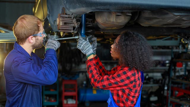 Eine junge Frau und ein junger Mann reparieren ein Auto in einer Werkstatt