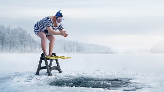 Mann mit Übergewicht und Schnorchel steht vor Eisloch und will hinein springen