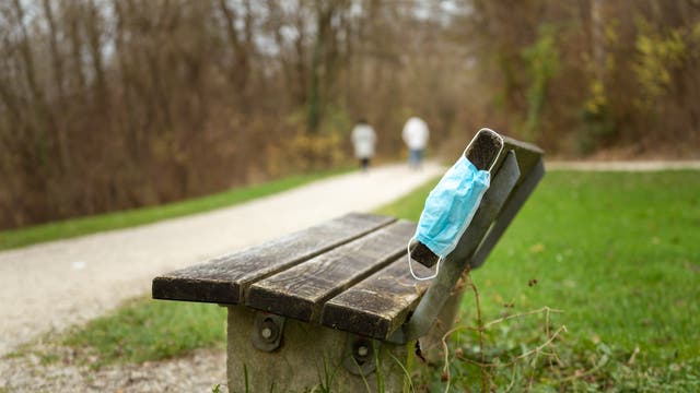An einer leeren Parkbank hängt ein zurückgelassener medizinischer Mund-Nasen-Schutz