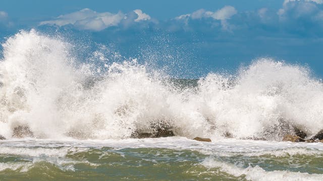 Eine Welle bricht an einem Wellenbrecher und erzeugt eine Gischtwolke.