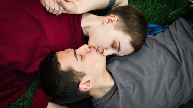 Mädchen und Junge im Teenageralter liegen auf einer Wiese und küssen sich  