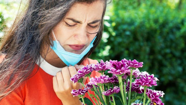 Frau mit Maske riecht an einer Blume