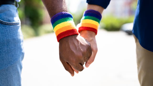 Ein schwules Paar hält einander an den Händen, am Handgelenk tragen sie Regenbogen-Bänder