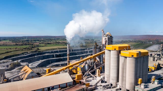 Luftaufnahme der Zementfabrik im industriellen Produktionsbereich. Rauch kommt aus dem Schornstein. 
