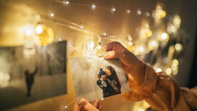 Familienfoto hängt an einer Lichterkette. Zwei Hände greifen danach.