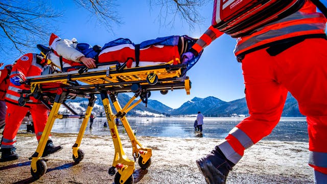 Zwei Sanitäter transportieren eine Person auf einer Trage an einem zugefrorenen See.