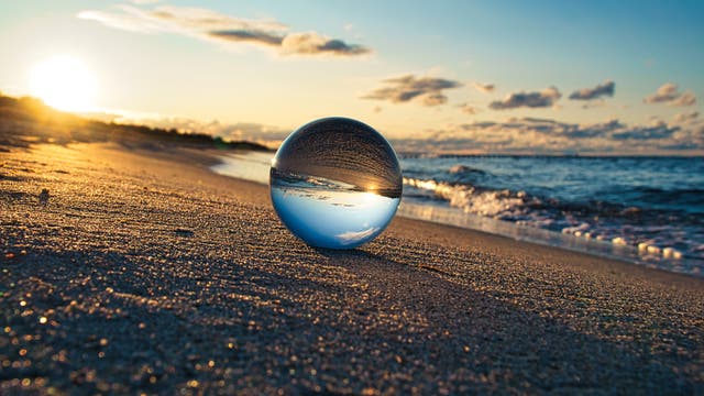 Eine Glaskugel am Ostseestrand, in der sich Strand und Meer spiegeln