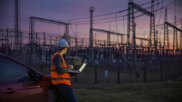Ein Arbeiter vor dem Netzanschluss eines großen Kraftwerks in der Abenddämmerung.