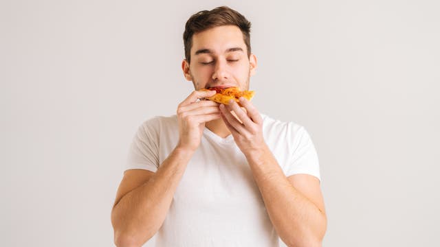 Ein junger Mann beißt mit genussvoll geschlossenen Augen in ein Stück Pizza.