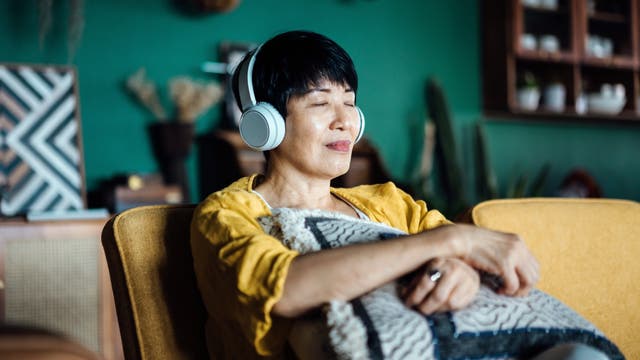 Asiatische Frau sitzt mit Kopfhörern und entspannter Mine auf dem Sofa in ihrer Wohnung.