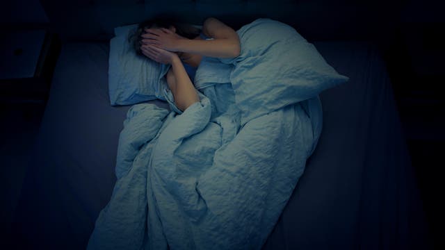 Frau liegt schlaflos im Bett und schlägt die Hände vors Gesicht.
