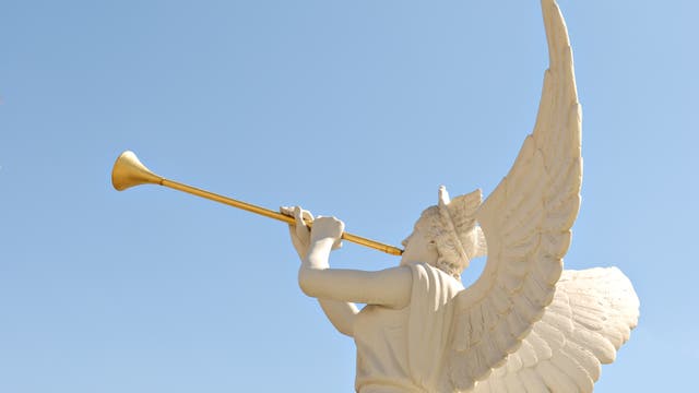 Eine Engelsstatue mit goldener Trompete gegen blauen Himmel fotografiert.