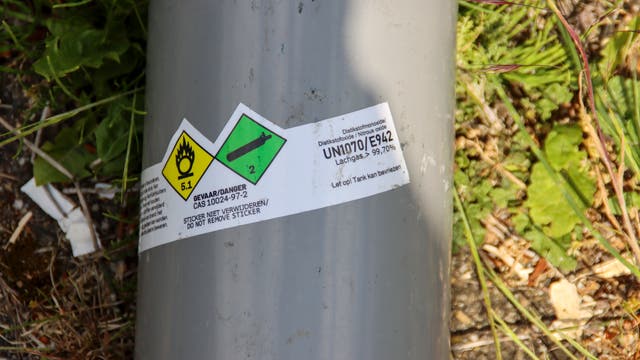 Eine große Lachgas-Kartusche mit Gefahrensymbolen liegt im Gras