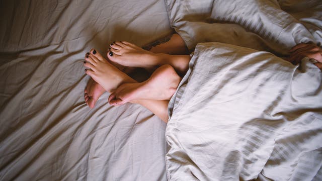 Zwei Paar Füße ragen unter der Bettdecke hervor - ein weibliches und ein männliches