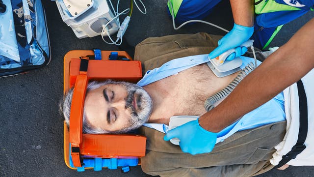Grauhaariger Mann liegt auf dem Boden und wird mit einem Defibrillator behandelt
