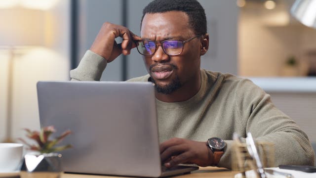 Ein Mann blickt auf den Bildschirm seines Laptops und wirkt verwirrt
