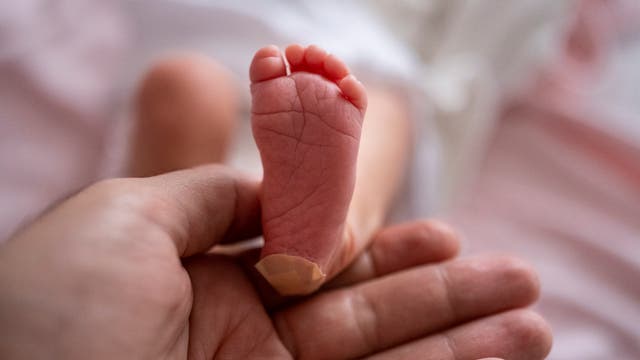 Fuß eines Neugeborenen, der von der Hand eines Mannes gehalten wird