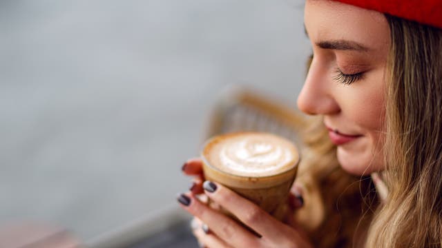 Eine Frau sitz in einem Café und riecht an einer Tasse Kaffee.