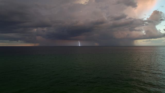 Ein Blitz zuckt aus einer Gewitterwolke über dem Meer.