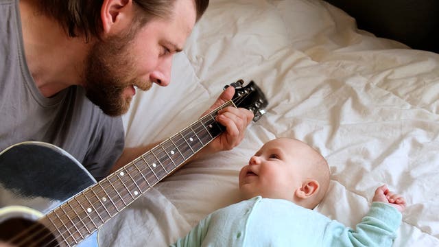 Ein Mann hat spielt ein Lied auf der Gitarre einem Baby vor, das ihn vergnügt anschaut.
