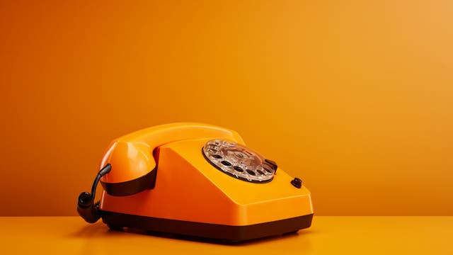 Organgenes Wählscheibentelefon vor orangenem Hintergrund