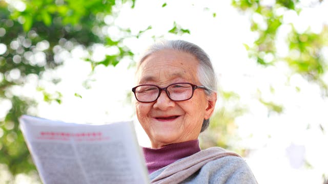 Ältere Dame liest hochvergnügt Zeitung.