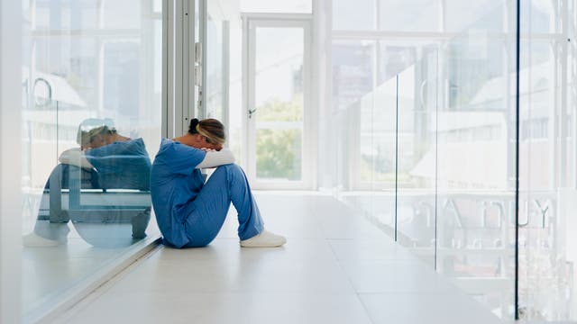 Im Flur eines Krankenhauses sitzt eine Ärztin oder Krankenschwester mit gesenktem Kopf auf dem Boden