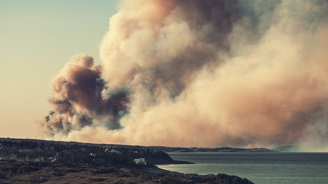 Rauch eines Waldbrandes steigt hoch über die Landschaft.