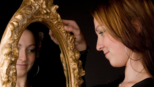 Eine Frau blickt glücklich in einen Spiegel.