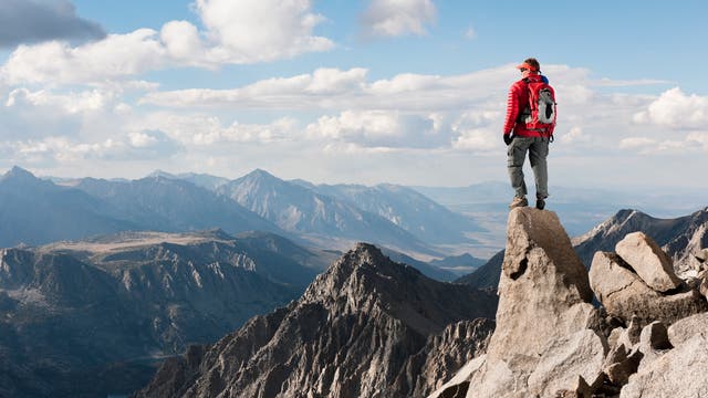 Ein Mann blickt von einem Berggipfel auf die umliegenden Berge 