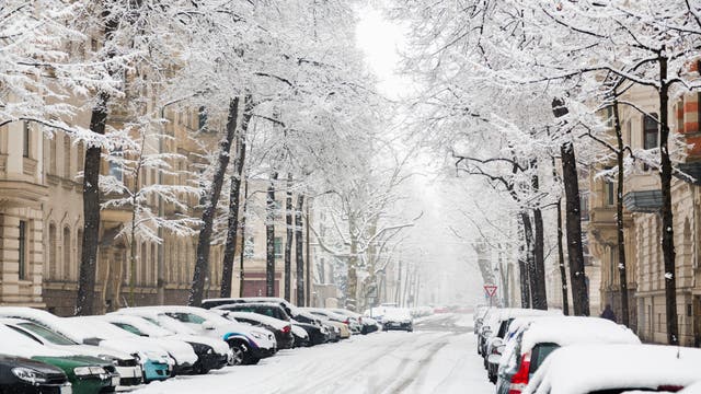 Eine verschneite Straße samt schneebedeckten Autos zwischen hübschen Altbauten.