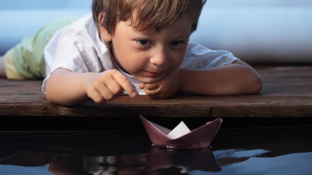 Ein kleiner Junge spielt mit einem Papierboot im Wasser