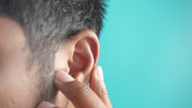 Nahaufnahme des Ohrs eines Mannes vor einem türkisen Hintergrund