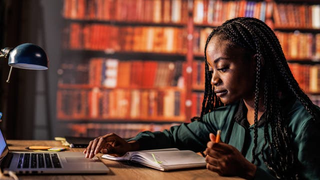 Eine junge Frau sitzt abends in einer Bibliothek und lernt