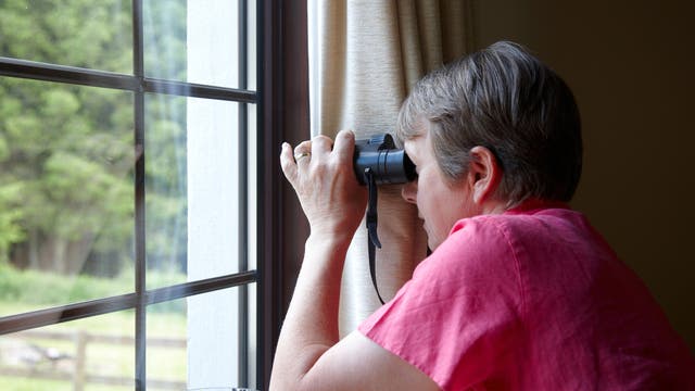 Frau schaut mit dem Fernglas aus dem Fenster