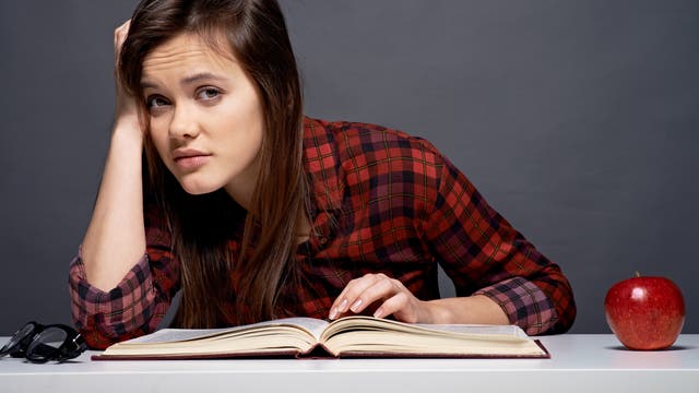 Jugendliche guckt beim Lernen genervt von ihrem Buch auf
