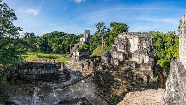 Blick von einer bin in mehrere Meter Höhe erhaltenen Maya-Ruine auf die Rasenfläche davor.