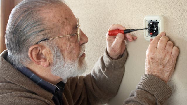 Ein älterer Herr steckt einen Schraubenzieher in eine offene Steckdose