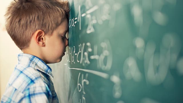 Ein Schüler lehnt mit dem Kopf an einer Tafel mit Mathe-Formeln.