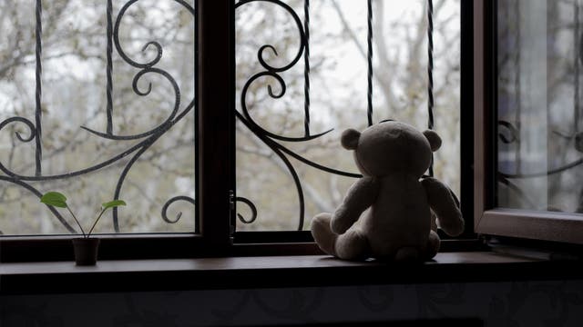 Teddybär sitzt am Fenster mit tristem Ausblick
