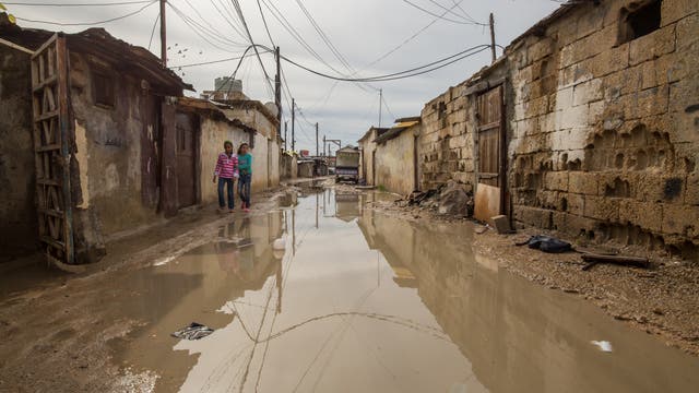 Wasser steht in einer Straße zwischen ärmlichen Behausungen.