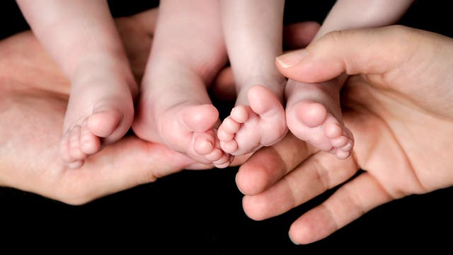 Zwei Hände von Erwachsenen, vier Babyfüße. Alle noch mit dem Körper verbunden.