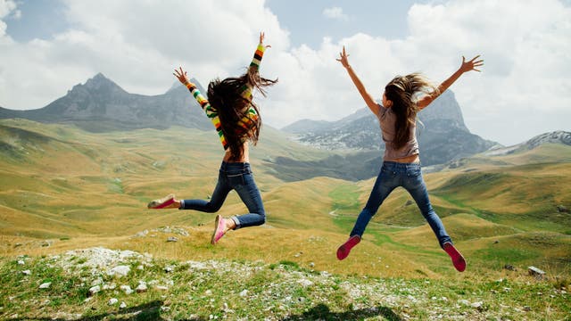 Zwei energiegeladene Mädchen springen vor einer Bergkulisse in die Höhe 