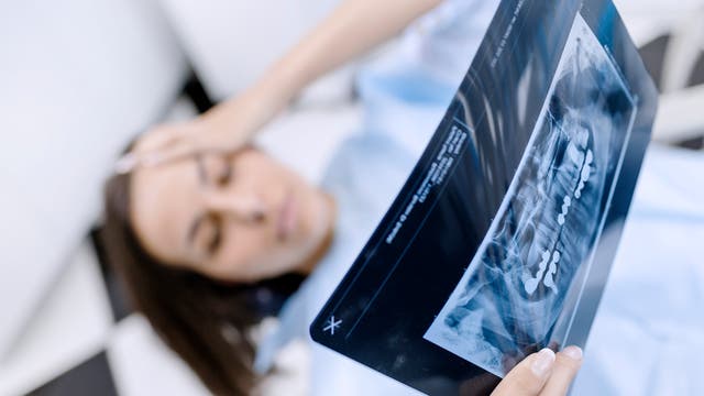 Schockierte Frau betrachtet Röntgenaufnahmen beim Zahnarzt