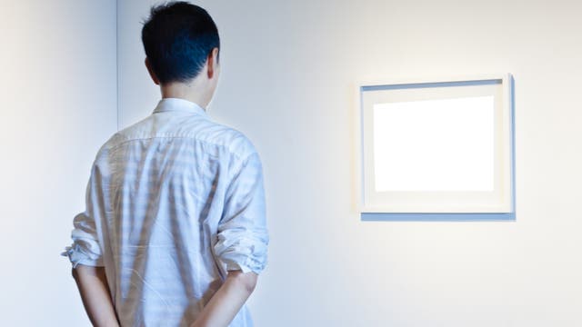 Ein Mann betrachtet Gemälde, auf denen nichts zu sehen ist.