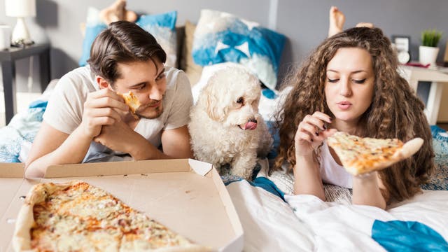 Paar liegt auf dem Bett und isst Pizza. Nein, das ist keine Netflix-Werbung. Nicht mal implizit.