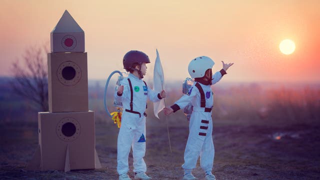 Zwei Kinder im Astronautenkostüm neben einer Rakete