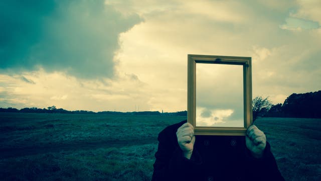 Eine Person hält einen Spiegel vor ihr Gesicht, so dass dieser ihren Kopf ersetzt.